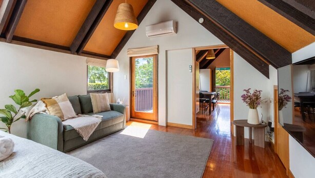 A cozy room with a sofa, a small table, and a plant. There is a door leading to another room with a table and chairs. - Merivale | King Bed + Carpark, Walk to Hagley Park (Christchurch)