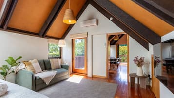 A cozy room with a sofa, a small table, and a plant. There is a door leading to another room with a table and chairs.