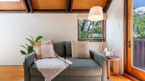 A cozy room with a green sofa, a hanging light fixture, and a view of greenery outside. - Merivale | King Bed + Carpark, Walk to Hagley Park (Christchurch)