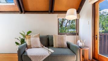 A cozy room with a green sofa, a hanging light fixture, and a view of greenery outside.