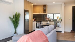 A modern kitchen with built-in appliances, a dining area with a table and chairs, and a grey sofa with a pink throw blanket. - 2-Bedroom Townhouse Opposite The Palms + Carpark (Christchurch)