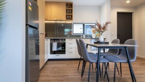 A modern kitchen with a built-in oven, a refrigerator, and a dining area with a table and chairs. - 2-Bedroom Townhouse Opposite The Palms + Carpark (Christchurch)