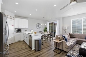 A modern kitchen with white cabinets, a stainless steel refrigerator, and a dining area with a table and chairs.