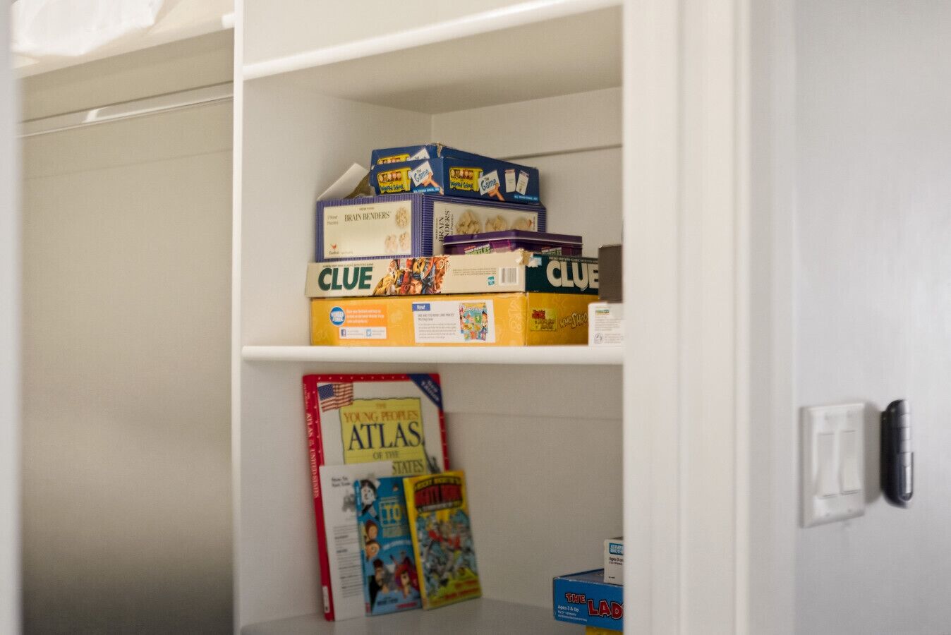 Une bibliothèque contenant divers jeux de société et un livre intitulé « L’atlas des États pour les jeunes ».