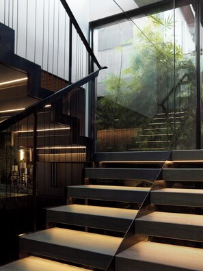 A modern staircase with glass railings and integrated lighting, leading to a second-floor area with a view of greenery outside. - Luxury Paddington Townhouse (Darlinghurst)