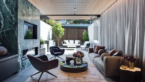 A modern living room with a marble wall, a round coffee table with decorative items, a sofa, and a TV mounted on the wall. - Luxury Paddington Townhouse (Darlinghurst)