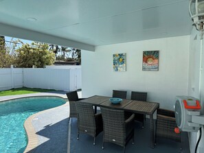 Une terrasse couverte avec une piscine, du mobilier d’extérieur et deux tableaux accrochés au mur.