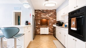 A modern kitchen with white cabinets, a brick backsplash, a black oven, and a bar area with stools. - Luxury Pool Home, Near the Beach and Cruise Port (Dania Beach)