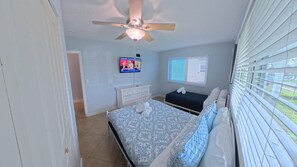 Een slaapkamer met een bed, een televisie, een dressoir en een raam met jaloezieën.