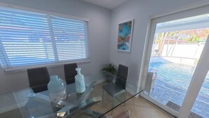 A modern dining area with a glass table, chairs, and a view of an outdoor swimming pool. - Luxury Pool Home, Near the Beach and Cruise Port (Dania Beach)