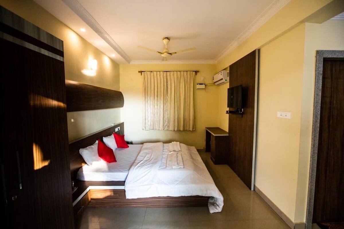 Una camera d'albergo con un letto, una ventola a soffitto, una televisione e una finestra con tende.