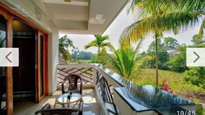 A balcony with a glass table and chairs, overlooking a lush garden with palm trees. - Eufregina Resort & Spa (Cavelossim)