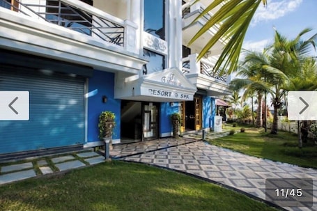 A resort with a blue facade, a sign reading "Resort & Spa," and a paved entrance area with palm trees.