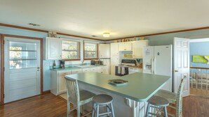 A kitchen with a central island, bar stools, a refrigerator, and a stove. - FSU Football, Fall Breezes & Scalloping Adventures (Alligator Point)
