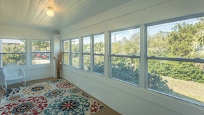 A room with large windows, a white chair, and a colorful rug. - FSU Football, Fall Breezes & Scalloping Adventures (Alligator Point)