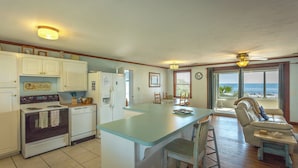 A kitchen with a large island, a dining area with a view of the ocean, and a living room with a sofa and chairs. - FSU Football, Fall Breezes & Scalloping Adventures (Alligator Point)