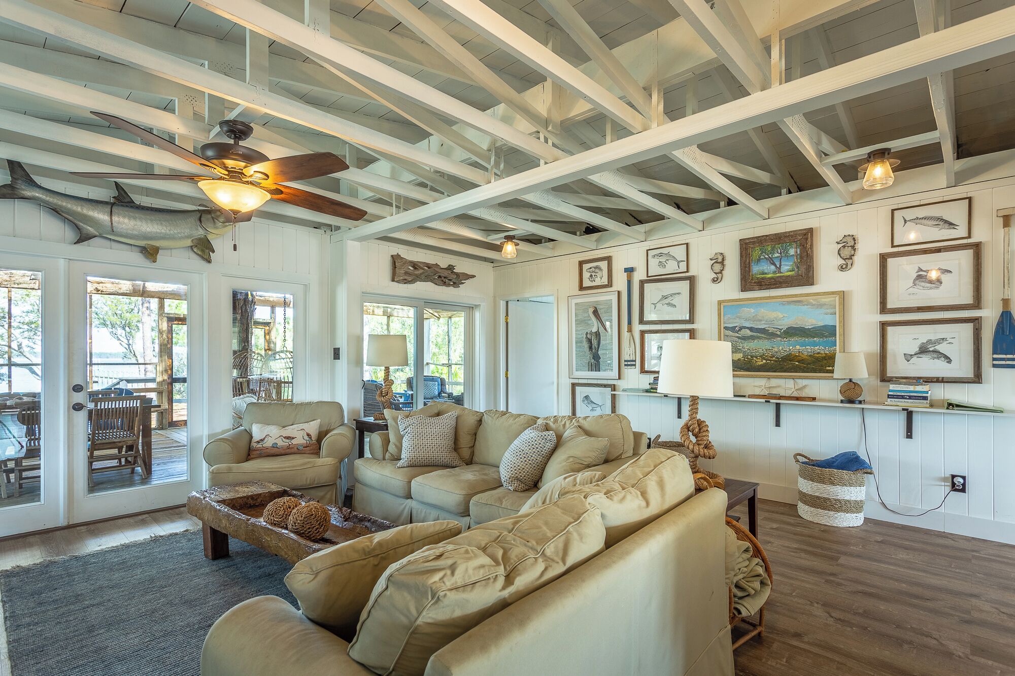 A spacious living room with a high ceiling and exposed beams, featuring a large beige sofa, a coffee table, and a ceiling fan.