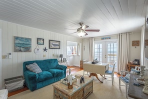 A cozy living room with a teal sofa, wooden coffee table, and a ceiling fan. - Gulf-Front Getaway | Nature, Privacy & Endless Views (Alligator Point)