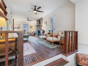 A cozy living room with a fireplace, wooden flooring, and a staircase leading to another level. - 5-Star Elegant 4BR: Fresh Reno, Superb View & Clean (Maggie Valley)