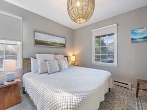 A bedroom with a large bed, a bedside table, a lamp, and a window with a view. - 5-Star Elegant 4BR: Fresh Reno, Superb View & Clean (Maggie Valley)