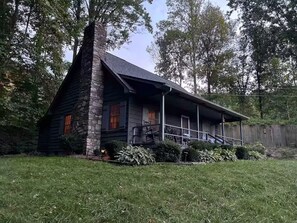 A rustic cabin with a stone chimney, a porch with outdoor seating, and a well-maintained lawn. - 5-Star Elegant 4BR: Fresh Reno, Superb View & Clean (Maggie Valley)