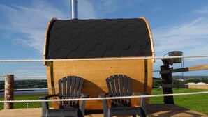 Una cabaña de madera con chimenea, dos sillas Adirondack y una barrera de cuerda.
