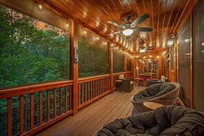Una terraza de madera con techo de ventilador, luces colgantes y mobiliario de mimbre.
