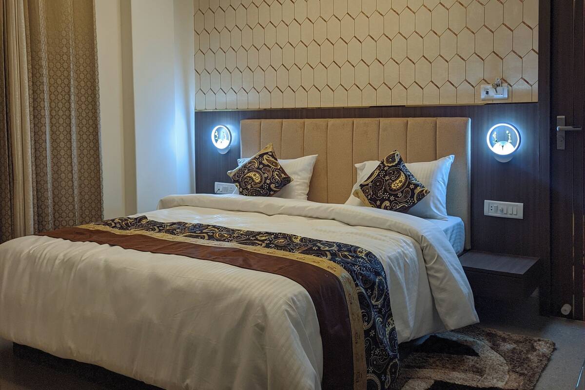 A modern hotel room with a large bed, a ceiling fan, a geometric-patterned wall, and a bedside table with a circular light.
