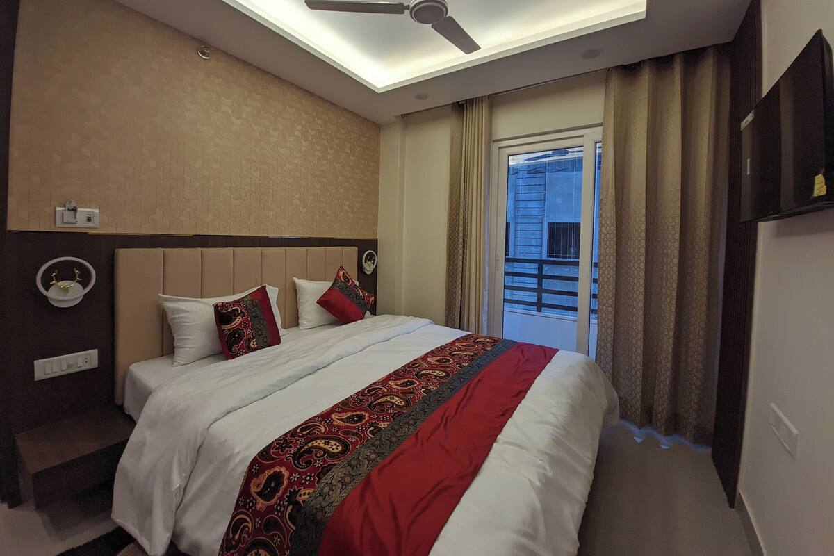 A hotel room with a bed, ceiling fan, and a view of the outside balcony.