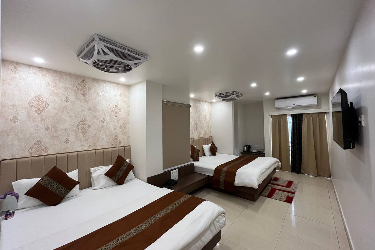 A hotel room with two beds, a TV mounted on the wall, an air conditioning unit, and a window with curtains.