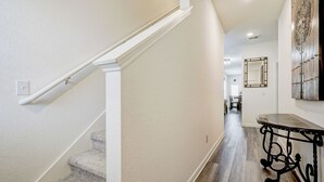 Un pasillo con una escalera alfombrada, un comedor al fondo y un espejo decorativo en la pared.