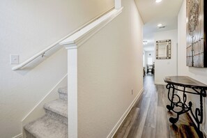 A hallway with a carpeted staircase, a dining area in the background, and a decorative mirror on the wall. - Texas Star / Big Texas Charm, Cozy Comfort (San Antonio)