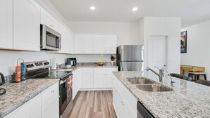 Una cocina moderna con armarios blancos, encimeras de granito, electrodomésticos de acero inoxidable y piso de madera.
