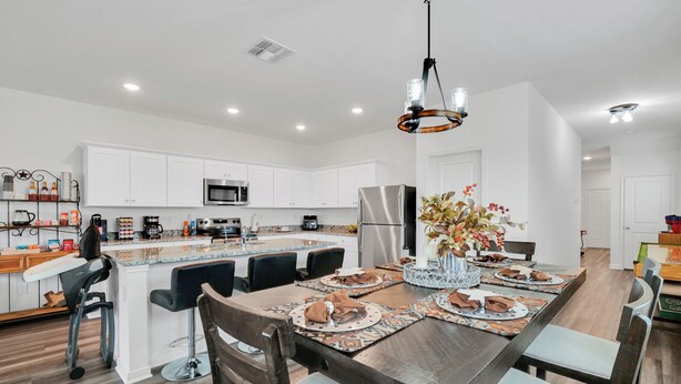 Una cocina moderna con armarios blancos, electrodomésticos de acero inoxidable y un comedor para seis personas con una mesa de madera y taburetes de bar.