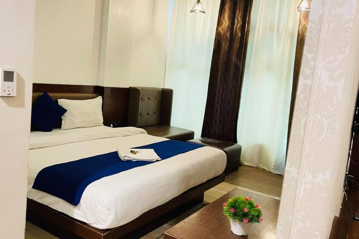 Ein Hotelzimmer mit Bett, Nachttisch, kleiner Topfpflanze und Wandthermostat.