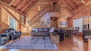A log cabin interior with a wooden staircase, leather furniture, and a dining area. - Labor Day & Fall Getaway, Epic Mountain Views, Hot Tub, Near Dollywood (Sevierville)