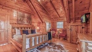 A log cabin interior with a bed, a red armchair, a television, and a cowhide rug. - Labor Day & Fall Getaway, Epic Mountain Views, Hot Tub, Near Dollywood (Sevierville)