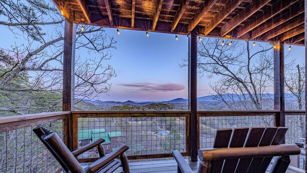 A wooden deck with two Adirondack chairs facing a scenic view of mountains and a green building in the distance. - Labor Day & Fall Getaway, Epic Mountain Views, Hot Tub, Near Dollywood (Sevierville)