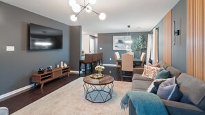 A modern living room with a large flat-screen TV, a wooden coffee table, and a sofa with multiple cushions.