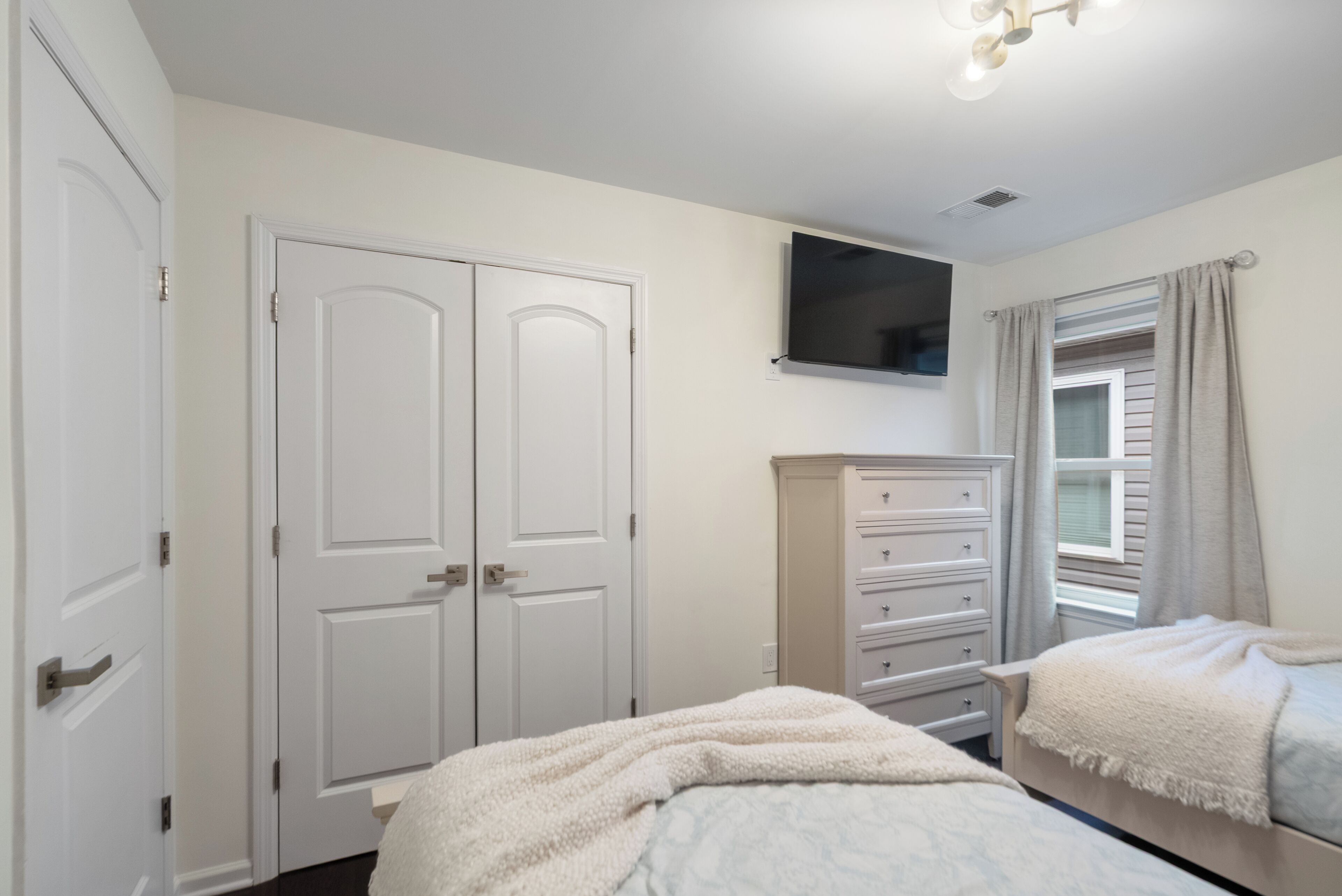 A bedroom with a bed, a dresser, a TV, and a window with curtains.