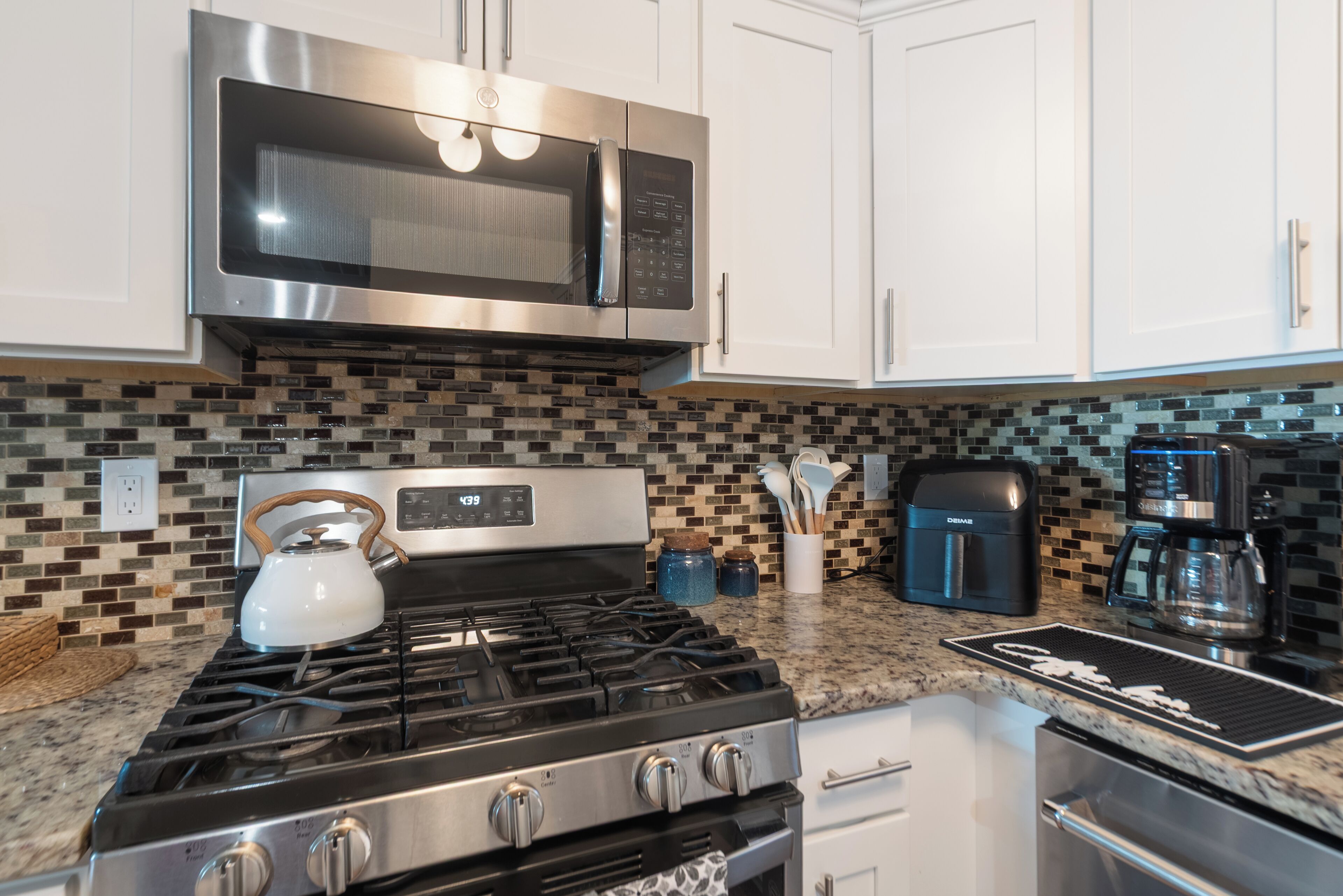 A kitchen with a gas stove, stainless steel microwave, and coffee maker.