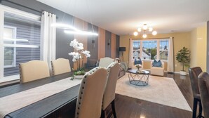 A modern dining area with a long table, chairs, and a chandelier.
