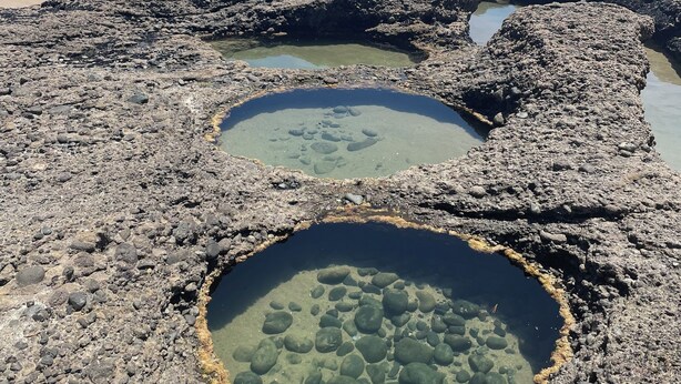 A rocky beach with two clear pools surrounded by black rocks.