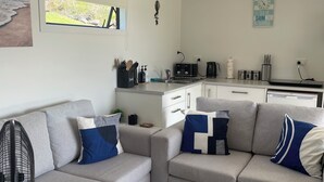 A modern living room with a grey sectional sofa, a standing fan, and a view of the kitchen area.
