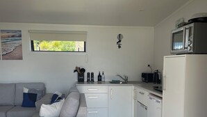 A modern kitchen with white cabinets, a microwave, and a refrigerator. There is a window with a view of greenery outside.