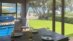 An outdoor dining area with a grill, table set for two, and a view of the ocean.