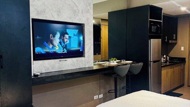 A modern hotel room with a TV mounted on the wall, a kitchen area with a refrigerator and microwave, and two beds with white bedding. - Twin Bed Near Airport, Mall of Asia, (Pasay City)