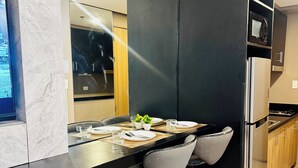 A modern kitchen with a black countertop, stainless steel appliances, and a wooden dining area with bar stools. - Twin Bed Near Airport, Mall of Asia, (Pasay City)