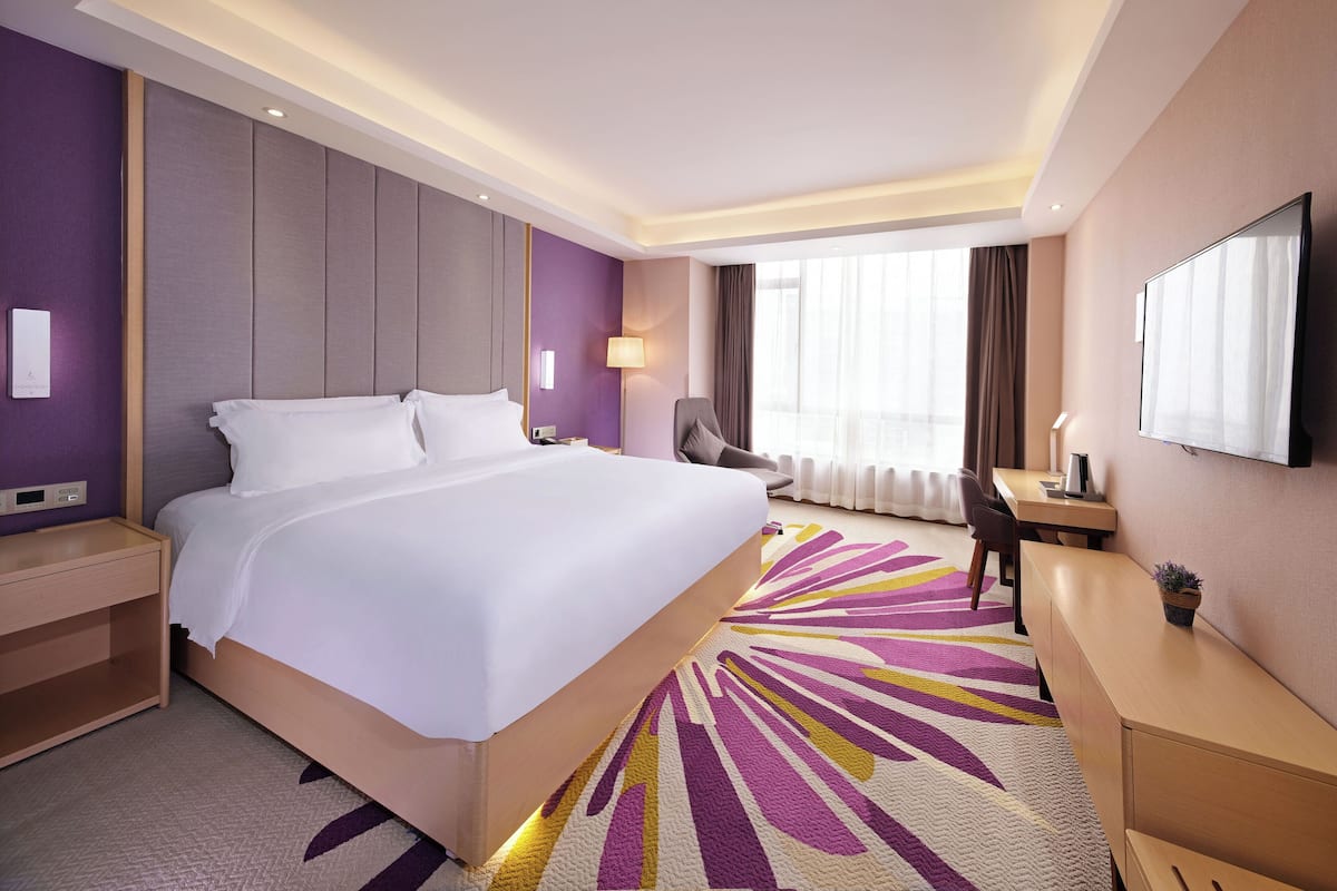 Quarto de hotel com uma cama grande, uma escrivaninha, uma cadeira e uma televisão.