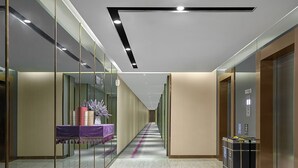 A modern hotel corridor with glass walls, a reception desk with a purple table, and an elevator on the right. - Lavande International Hotel Guangzhou Baiyun International Airport Renhe Metro Station Branch (Guangzhou)